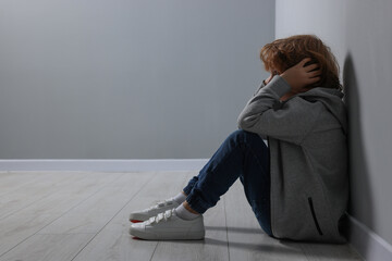 Child abuse. Upset boy sitting on floor near grey wall, space for text