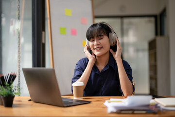 A focused professional woman listens to music with headphones, holding a coffee cup while taking a break at her workspace.
