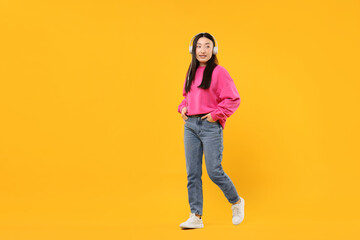 Fototapeta premium Portrait of smiling woman in headphones on orange background. Space for text