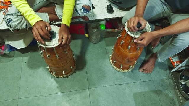 Two people sitting on the floor playing traditional drums with a focus on hands and instruments man repairing drum at musical workshop