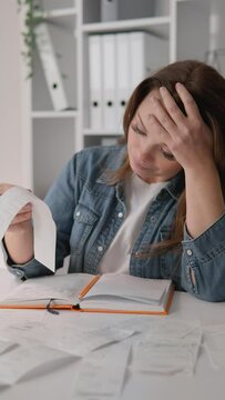 A vertical video showing a woman analyzing bills and calculating expenses with a notebook in concentration. She works from home, seriously managing the family budget and calculations
