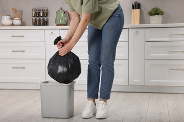 Woman taking garbage bag out of trash bin in kitchen, closeup