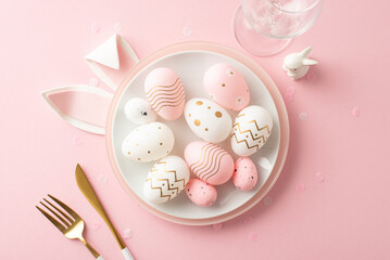 Glamorous Easter meal setting inspiration. Top view of cutlery, wineglass, plate, full of speckled eggs, rabbit statue, bunny ears and confetti on a pastel pink surface