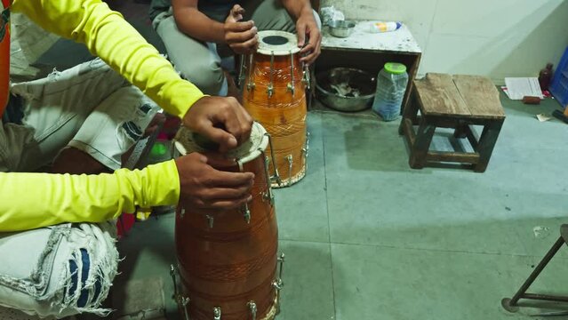 Two people sitting and tuning traditional Indian tabla drums with focus on the instruments and hands man repairing drum at musical workshop