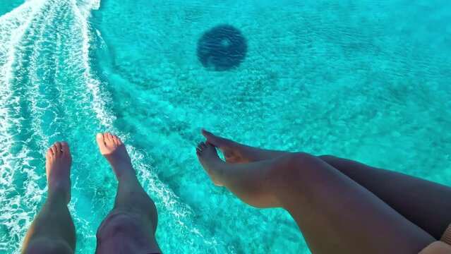 Two tourists parasailing behind a speedboat over an azure ocean.