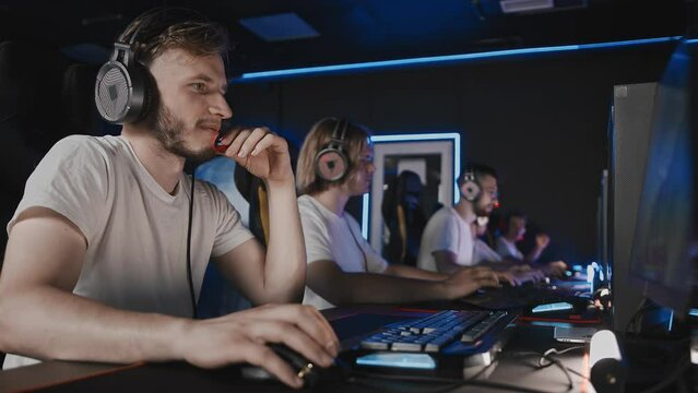 Gamers playing video game on PC at computer club, cyber sport tournament. E-sport championship. Five players in headset. Player talks to his team over mic. Multiplayer online, first-person shooter