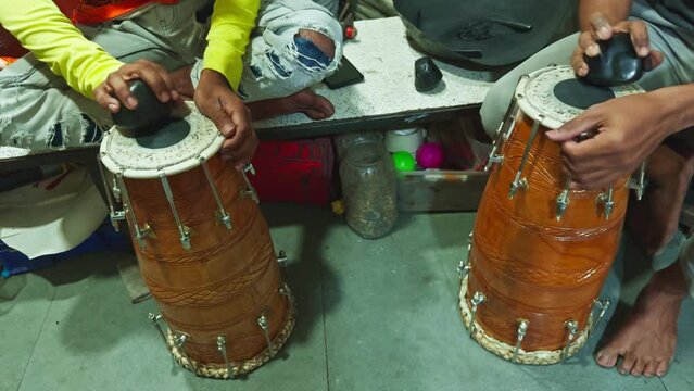 Two people sitting and playing traditional drums with their hands focus on the instruments and human interaction man repairing drum at musical workshop