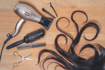 Hairdresser tools and piece of dark hair on the wooden background.