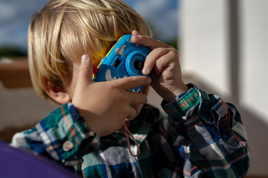 little blond boy takes pictures with a child's camera. People. A handsome funny and emotional blond man in a checkered shirt with a children's camera is taking pictures. Close-up.