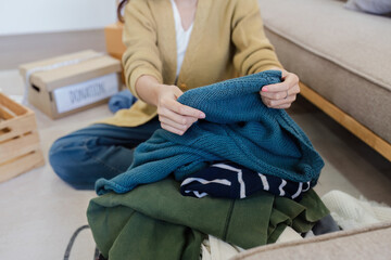 Young Asian women sit in living room sorting clothes for donation in a donation box second hand clothes