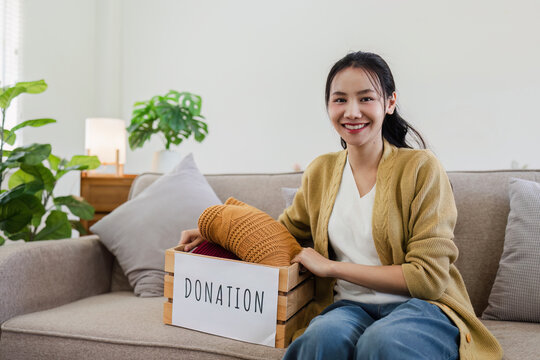 Young Asian women sit in living room sorting clothes for donation in a donation box second hand clothes