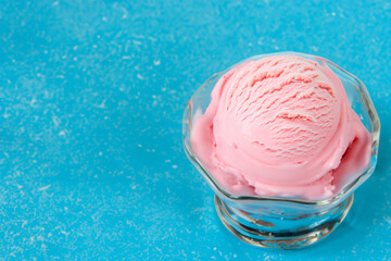 Scoop of pink ice cream in glass bowl on blue background