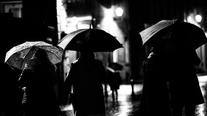 In a monochromatic scene, figures traverse the rain under umbrellas, capturing the timeless essence...