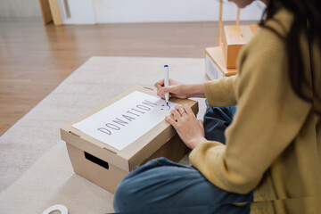 Asian woman sitting and writing on a box to prepare for donation. Help poor people - obrazy, fototapety, plakaty
