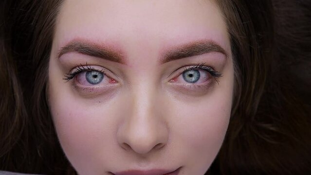 Chic young girl immediately after the permanent eyebrow makeup procedure, there is redness of the skin around the eyebrows. Permanent makeup procedure, performing PMU of eyebrows