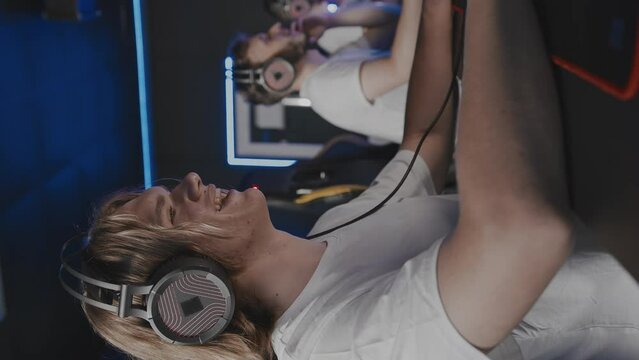 Focused laughing smiling pimply teen gamer in headset playing PC video game at computer club cyber sport tournament. E-sport championship. Multiplayer online strategy first-person shooter. Vertical