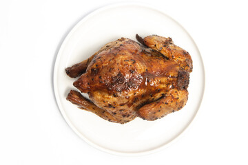 A whole delicious roasted chicken seasoned with herbs in a white plate top view isolated on white background clipping path