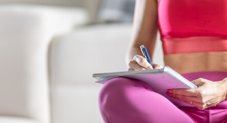 Sporty woman sits on a mat and writes down future training plans for achieving sports results - 748627092