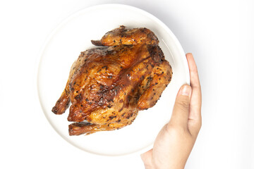 Hand holding a whole delicious roasted chicken seasoned with herbs in a white plate top view isolated on white background clipping path