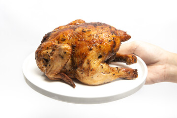 Hand holding a whole delicious roasted chicken seasoned with herbs in a white plate isolated on white background clipping path