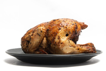 A whole delicious roasted chicken seasoned with herbs in a black plate isolated on white background...