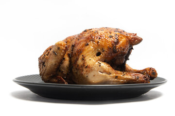 A whole delicious roasted chicken seasoned with herbs in a black plate isolated on white background clipping path