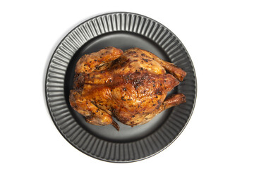 A whole delicious roasted chicken seasoned with herbs in a black plate top view isolated on white background clipping path
