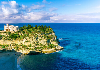 sea landscape of beautiful white temple or castle on a high cliff isle on a rock in crystal clear turquoise sea with waves and beautiful sunset or sunrise on background of seascape