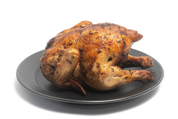 A whole delicious roasted chicken seasoned with herbs in a black plate isolated on white background clipping path