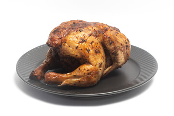 A whole delicious roasted chicken seasoned with herbs in a black plate isolated on white background clipping path