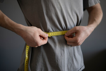 Man Measures Waist Circumference With Yellow Tape During Fitness Check