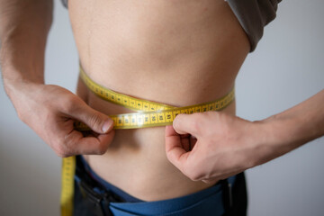 Man Measures Waist Circumference With Yellow Tape During Fitness Check