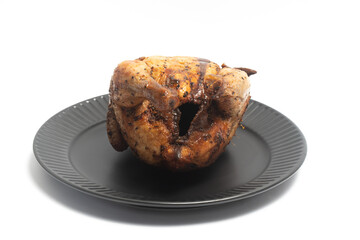 A whole delicious roasted chicken seasoned with herbs in a black plate isolated on white background clipping path