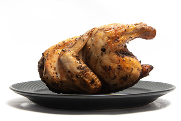 A whole delicious roasted chicken seasoned with herbs in a black plate isolated on white background clipping path