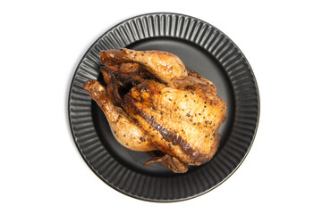 A whole delicious roasted chicken seasoned with herbs in a black plate top view isolated on white background clipping path