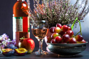 ripe grapes with a glass of wine with an apple with plums and flowers