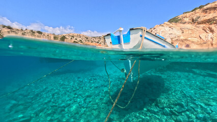 Underwater split photo of traditional fishing boat anchored in small secluded fjord and paradise...