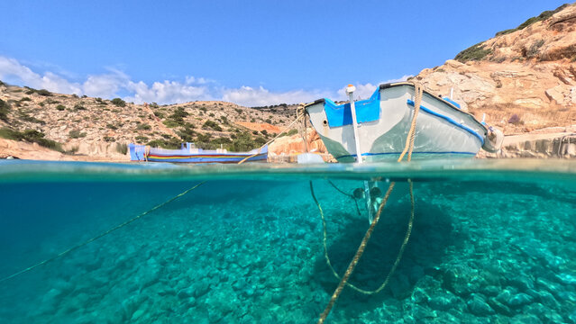 Underwater split photo of traditional fishing boat anchored in small secluded fjord and paradise beach of Tourkopigado, Iraklia island, Small Cyclades, Greece