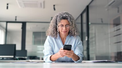 Happy middle aged business woman holding mobile cell phone using cellphone in office. Smiling mature older professional lady business owner entrepreneur using smartphone working sitting at desk. - Powered by Adobe