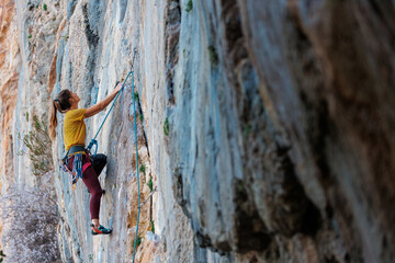 A woman climbs a rock, a strong girl trains strength and endurance, extreme sport, rock climbing..