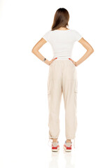 Cute brunette woman in white shirt and loose white trousers posing on a white background. Full...