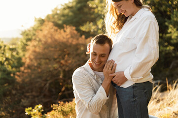 a pregnant woman and a young husband are hugging while holding an ultrasound scan near the pregnant belly. happy family concept. pregnant family on a walk. close-up