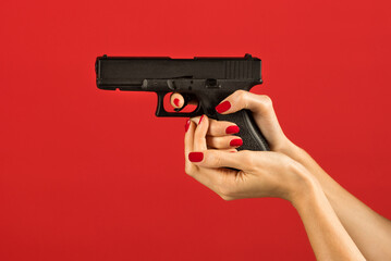Anonymous female hand holding pistol on red backdrop