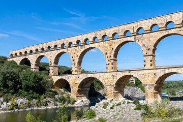 Low angle view of the aqueduct bridge Pont du Gard over the Gardon river near Vers-Pont-du-Gard, France with well-preserved arched tiers, built by 1st-century Romans - obrazy, fototapety, plakaty
