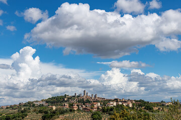 Panoramic view of skyline of walled medieval hill town San Gimignano in Tuscany, Italy known as the Town of Fine Towers famous for its medieval architecture of tower houses with dramatic clouded sky - obrazy, fototapety, plakaty