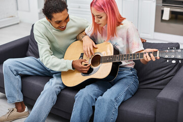 handsome jolly african american man teaching his girlfriend how to play guitar while at home
