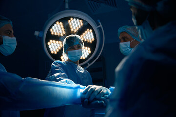 Surgeons holding hands while preparing for operation in operating room - obrazy, fototapety, plakaty