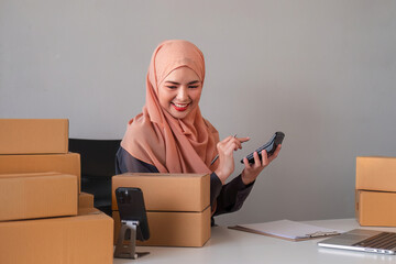 Asian Muslim businesswoman checks stock orders and saves them on her home office laptop. small business owner Shipping in online markets The concept of freedom in life - obrazy, fototapety, plakaty