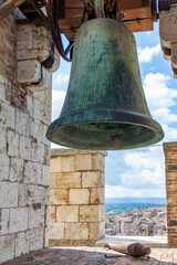 Fototapeta premium Close up view of the bell and clapper in the top of the tallest tower Torre Grossa in San Gimignano, Italy with the city buildings and Tuscan landscape seen through the crenel of wall