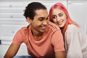 focus on cheerful african american man in homewear smiling at his blurred pink haired girlfriend